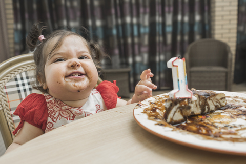 Cute girl with messy face having birthday cake at table stock photo