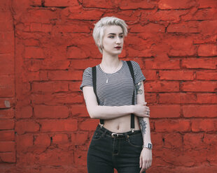 Selbstbewusste junge Frau, die an einer roten Backsteinmauer steht - FSIF01668