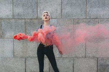 Confident young woman standing with distress flare against wall - FSIF01669