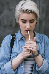 Junge modische Frau, die im Freien stehend eine Zigarette raucht - FSIF01676
