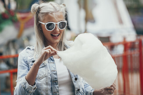 Modische junge Frau mit Sonnenbrille beim Essen von Zuckerwatte im Freien - FSIF01681