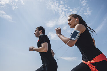 Low angle view of young man and woman jogging against sky - FSIF01686