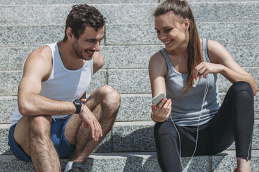 Cheerful woman showing smart phone to male friend while sitting on steps - FSIF01690
