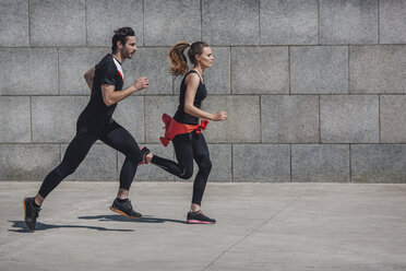 Side view of people jogging on sidewalk by wall - FSIF01692