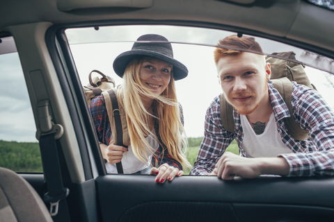 Lächelnde männliche und weibliche Rucksacktouristen schauen in ein Autofenster, lizenzfreies Stockfoto