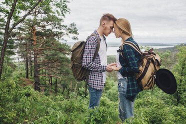 Loving couple holding hands while standing amidst plants at forest - FSIF01705