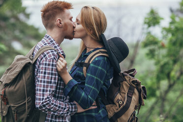 Verliebtes Paar mit Rucksäcken, das sich küsst, während es im Wald steht - FSIF01713