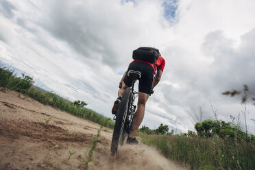 Low angle view of man riding mountain bike on dirt road against cloudy sky - FSIF01717