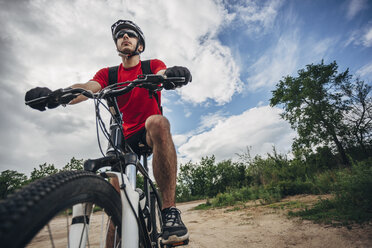 Low angle view of mountain biker riding on dirt road against sky - FSIF01721