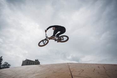 Niedriger Blickwinkel auf einen Teenager, der einen Stunt beim BMX-Radfahren vor bewölktem Himmel ausführt - FSIF01731