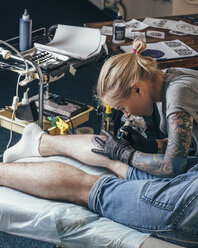 Artist tattooing design on man's leg at studio - FSIF01735