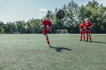 Fußballspieler kickt den Ball, während Freunde in der Nähe auf dem Feld stehen - FSIF01746