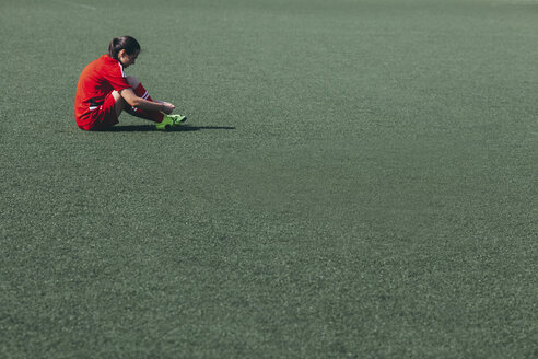 Side view of soccer player sitting on playing field - FSIF01748
