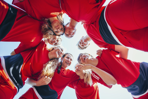 Cheerful soccer players talking while huddling against clear sky stock photo