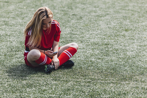 Fußballspieler benutzt sein Smartphone, während er auf dem Feld sitzt, lizenzfreies Stockfoto