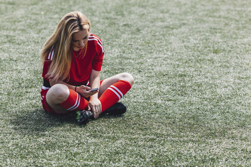 Soccer player using smart phone while sitting on field - FSIF01755