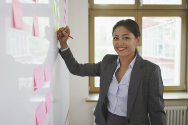 Confident businesswoman writing on adhesive note at creative office - FSIF01765