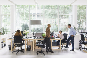 Businesswoman working at desk while colleagues discussing in meeting - FSIF01772