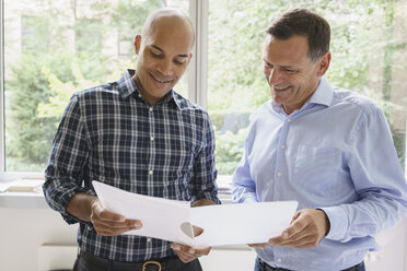 Smiling businessmen discussing over file against window at creative office - FSIF01776