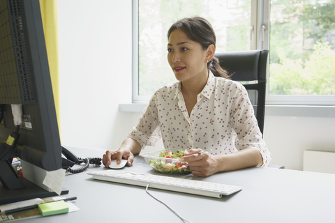 Geschäftsfrau mit Computer und Salat im Kreativbüro, lizenzfreies Stockfoto