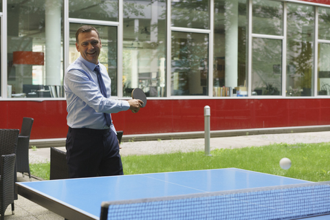 Selbstbewusster glücklicher Geschäftsmann spielt Tischtennis im Kreativbüro, lizenzfreies Stockfoto