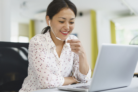 Smiling businesswoman using headphones and laptop at office desk stock photo