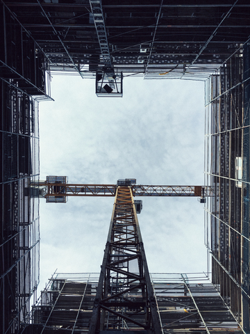 Unmittelbar unter der Aufnahme eines Krans inmitten eines Glasgebäudes gegen den Himmel, lizenzfreies Stockfoto