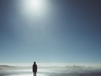 Rear view of silhouette woman looking at demolished city against clear sky on sunny day - FSIF01804