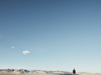Rear view of man standing on barren landscape against blue sky, San Bernardino, California, USA - FSIF01809