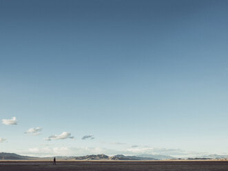 Entfernte Ansicht eines Mannes, der auf einem Feld zwischen Bergen gegen den Himmel läuft, Zzyzx, Kalifornien, USA - FSIF01811