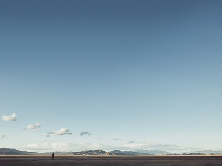 Entfernte Ansicht eines Mannes, der auf einem Feld zwischen Bergen gegen den Himmel läuft, Zzyzx, Kalifornien, USA - FSIF01811