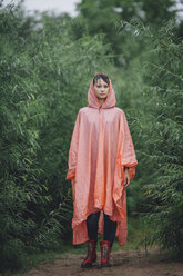Porträt einer Frau mit Regenmantel inmitten von Pflanzen während der Regenzeit - FSIF01820