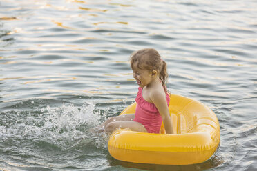 Fröhliches Mädchen sitzt auf einem Floß und spielt im See - FSIF01824