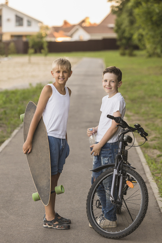Lächelnde Freunde mit Skateboard und Fahrrad stehen im Park, lizenzfreies Stockfoto