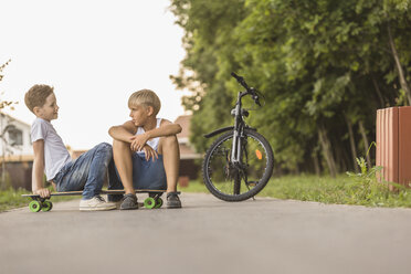 Freunde unterhalten sich auf dem Skateboard sitzend mit dem Fahrrad im Park - FSIF01828