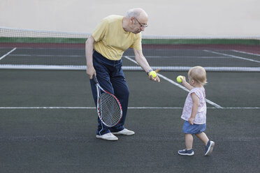 Mädchen, das seinem Großvater einen Tennisball schenkt, während es auf einem Spielfeld steht - FSIF01830