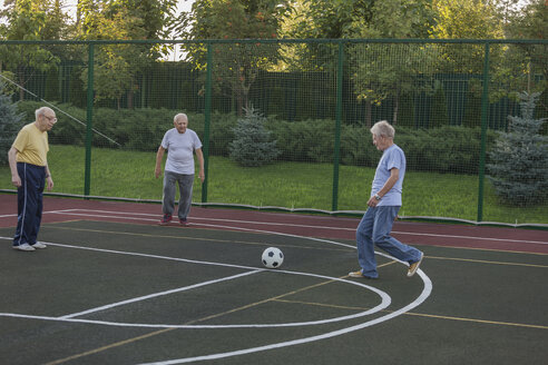 Ältere Freunde spielen Fußball am Zaun auf einem Feld - FSIF01833