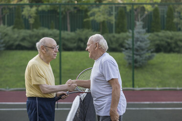 Ältere Freunde schütteln sich über dem Netz auf dem Tennisplatz die Hände - FSIF01834