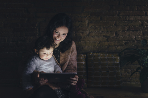 Mutter und Tochter benutzen ein digitales Tablet zu Hause im Dunkeln, lizenzfreies Stockfoto