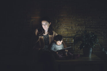 Mutter und Tochter benutzen zu Hause im Dunkeln ein Mobiltelefon und ein digitales Tablet - GEMF01886