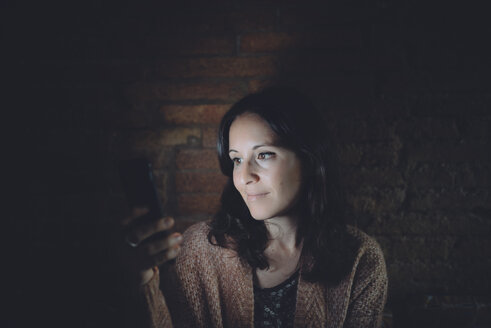 Porträt einer Frau, die zu Hause in der Dunkelheit ihr Smartphone benutzt - GEMF01887