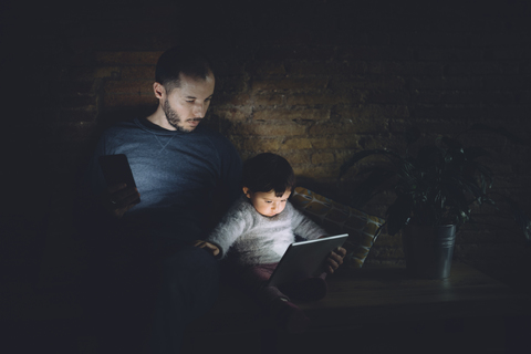 Vater und Tochter schauen zu Hause im Dunkeln auf ein digitales Tablet, lizenzfreies Stockfoto