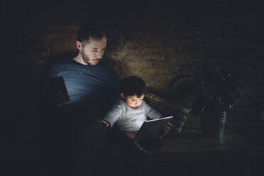 Vater und Tochter schauen zu Hause im Dunkeln auf ein digitales Tablet - GEMF01888