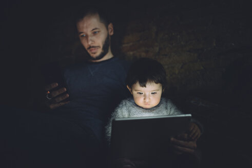 Vater und Tochter nutzen Phablet und digitales Tablet zu Hause im Dunkeln - GEMF01889