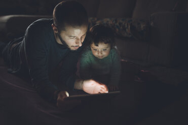Father and daughter looking at digital tablet at home in the dark - GEMF01890