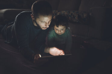 Vater und Tochter schauen zu Hause im Dunkeln auf ein digitales Tablet - GEMF01890