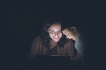 Mother and daughter using digital tablet at home in the dark - GEMF01891