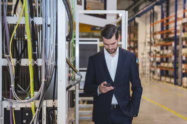 Geschäftsmann in einer Fabrik, der sein Mobiltelefon überprüft - DIGF03388