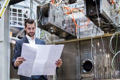 Businessman in factory looking at plan stock photo