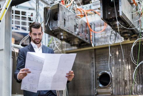 Geschäftsmann in einer Fabrik mit Blick auf einen Plan - DIGF03389